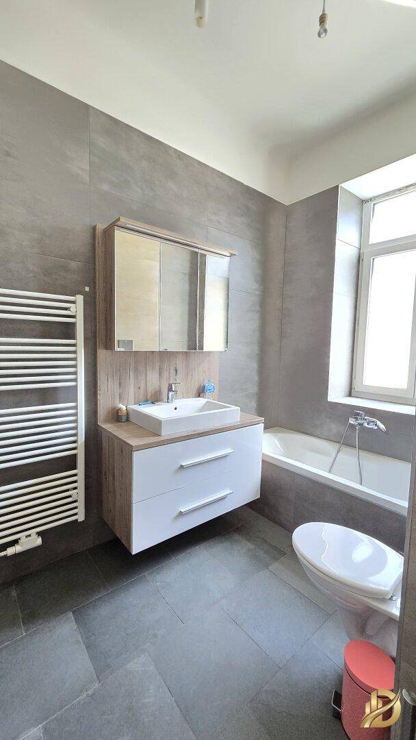 Modernes Badezimmer mit grauen Fliesen, Badewanne, Waschtisch und beheiztem Handtuchhalter.