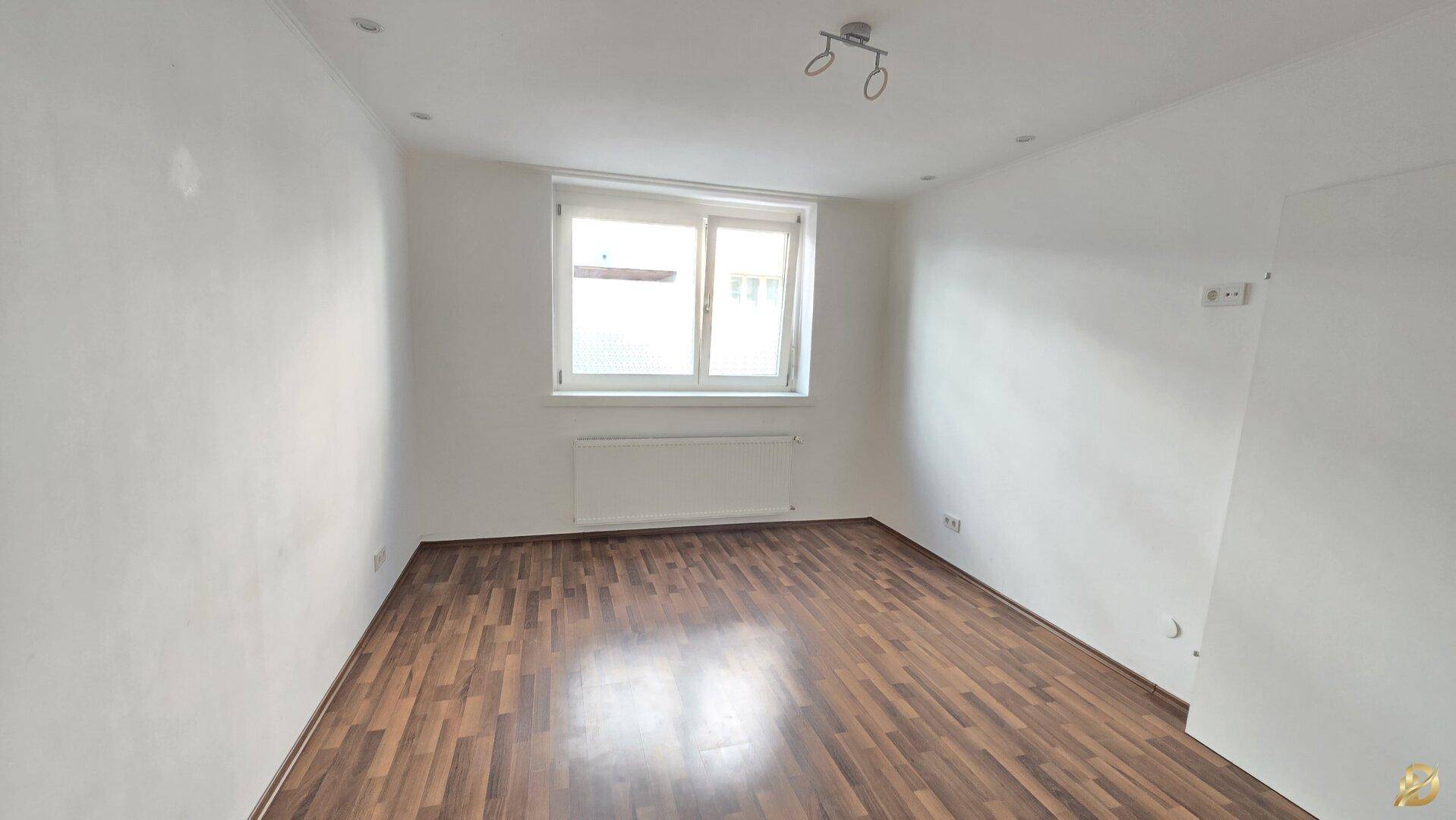 Geräumiges, helles Zimmer mit Parkettboden und einem großen Fenster.
