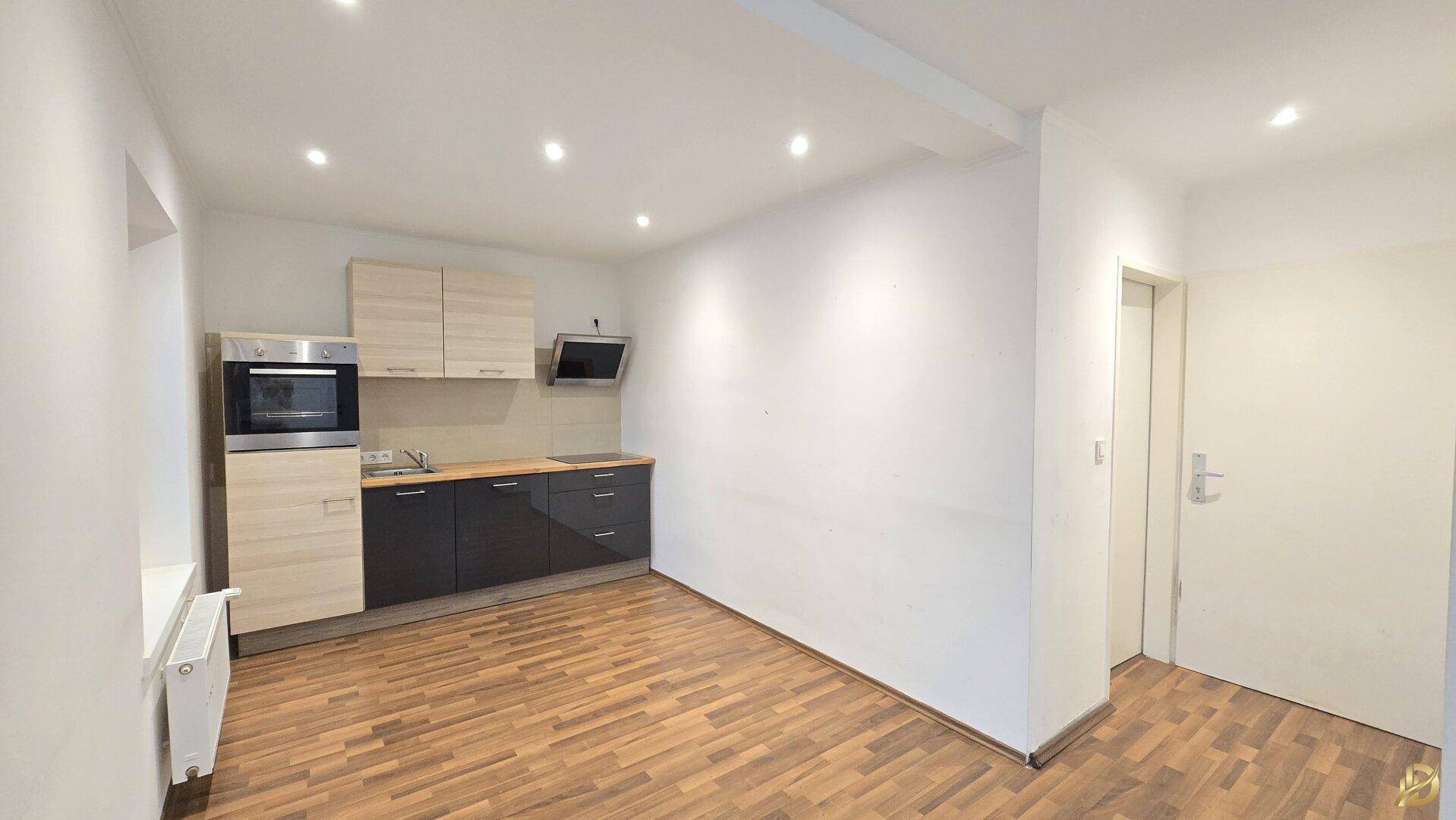 Moderne Küchenzeile mit Holz- und dunklen Fronten in einem hellen Wohnraum.