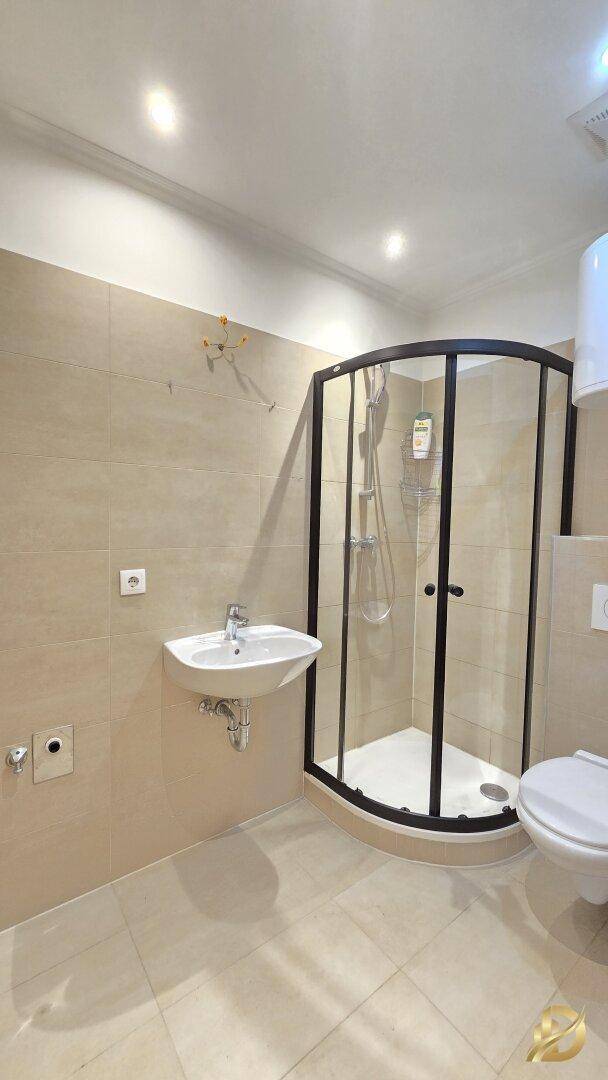 Modernes Badezimmer mit Duschkabine, Waschbecken und WC in hellen Beigetönen.