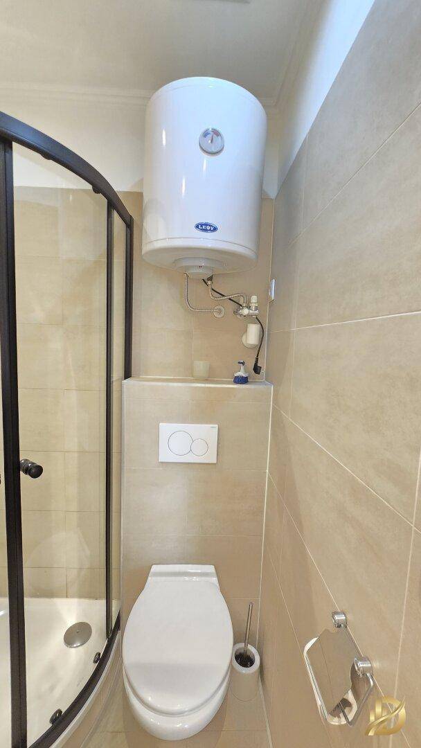 Wandhängendes WC mit Spülkasten und Warmwasserboiler in einem gefliesten Badezimmer.