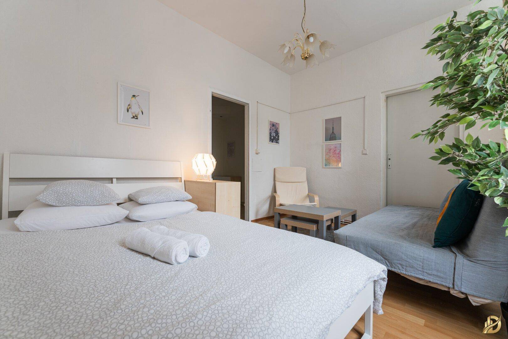 Schlafbereich mit Doppelbett und Schlafsofa, Holzboden und heller Einrichtung in einem gemütlichen Raum.