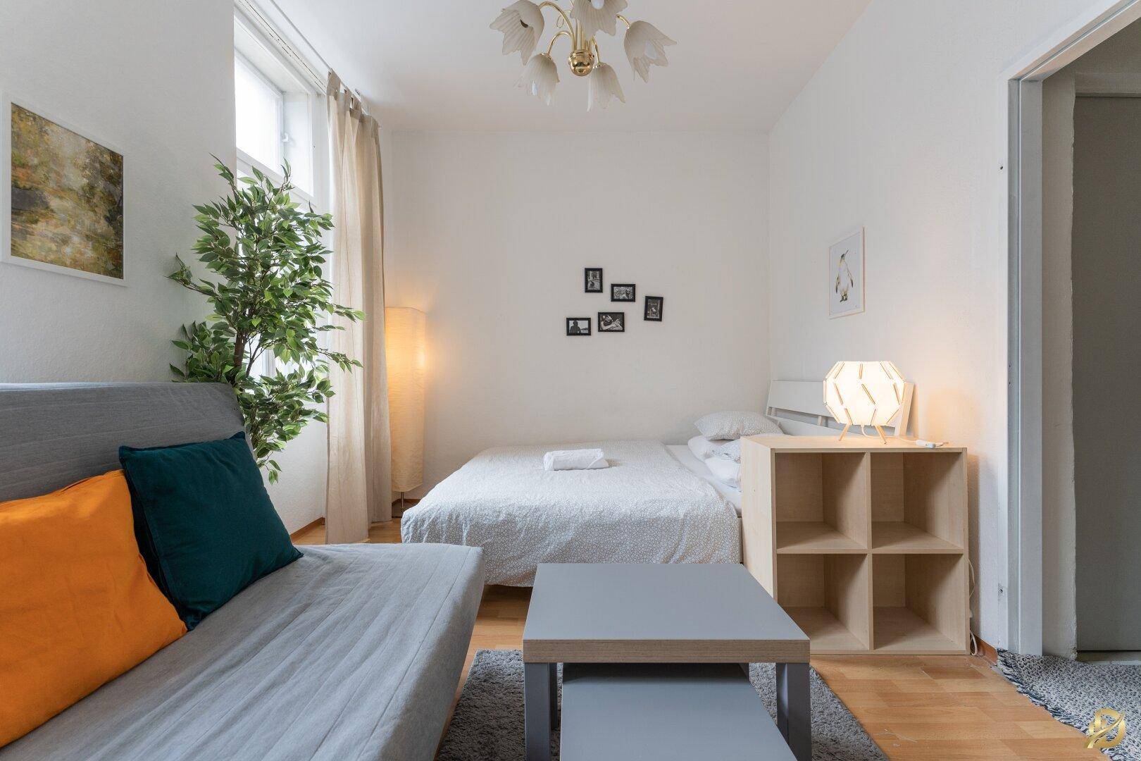 Gemütliches Wohnzimmer mit Schlafbereich, Holzboden und moderner Dekoration, gut beleuchtet.