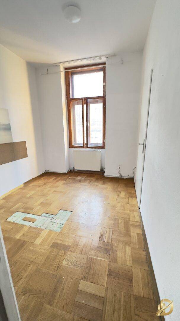 Leeres Schlafzimmer mit Parkettboden und einem Fenster, das Tageslicht hereinlässt.
