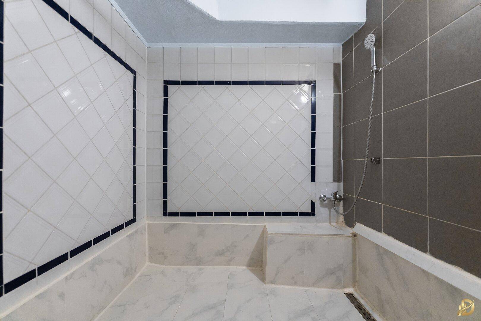 Badezimmer mit Duschbereich, weißen und grauen Fliesen, sowie einer Handbrause.