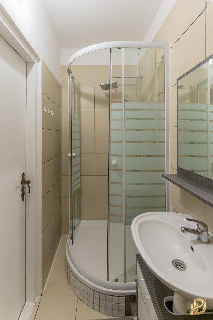 Badezimmer mit Duschkabine, Waschbecken und Spiegel, hell gefliest und funktional.