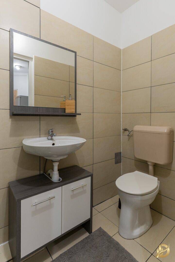 Badezimmer mit Waschbecken, Spiegel und Toilette, hell gefliest und sauber.