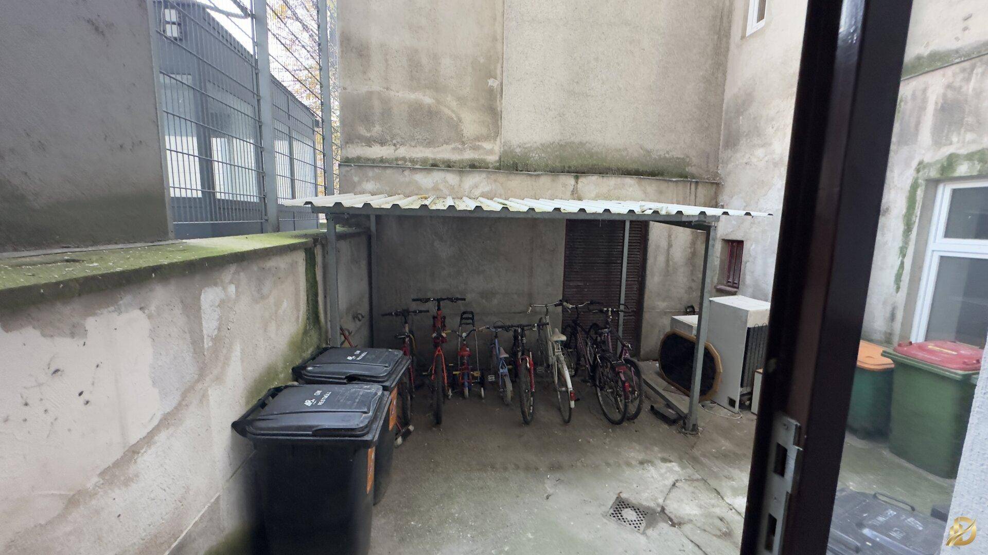 Hinterhof mit Fahrradunterstand und Mülltonnen, umgeben von alten Gebäuden.