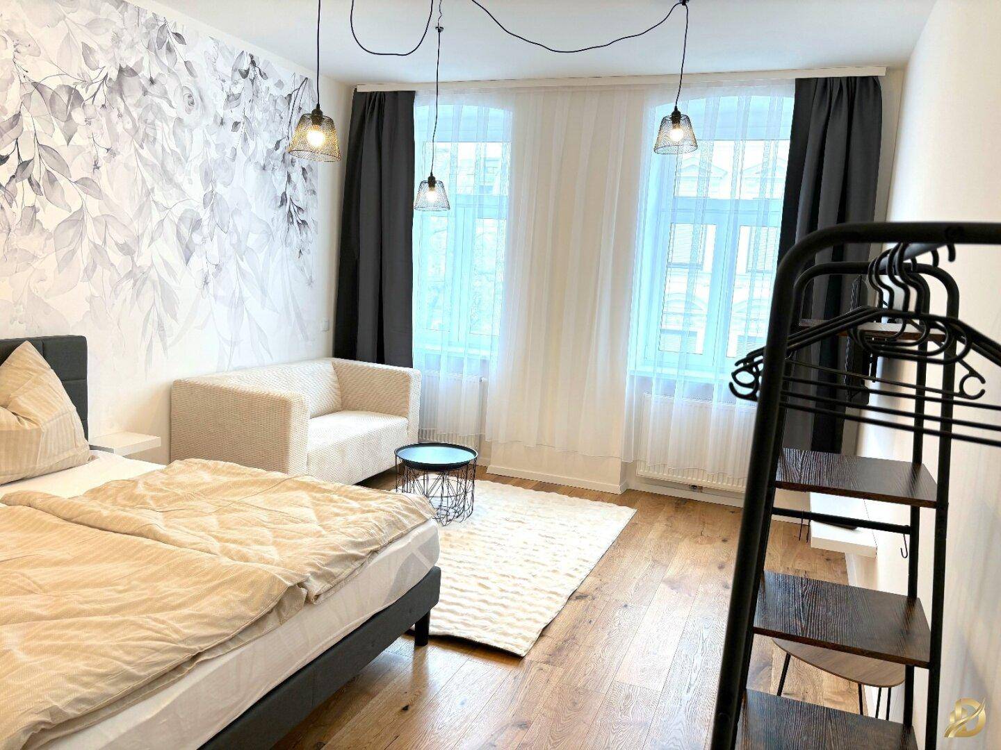 Heller Wohnbereich mit floraler Tapete, großen Fenstern und bequemer Couch.