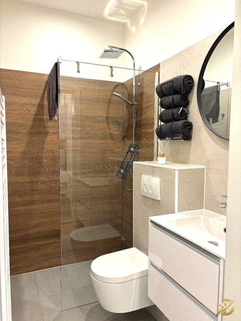 Modernes Badezimmer mit ebenerdiger Dusche, Hänge-WC und runden Spiegel.