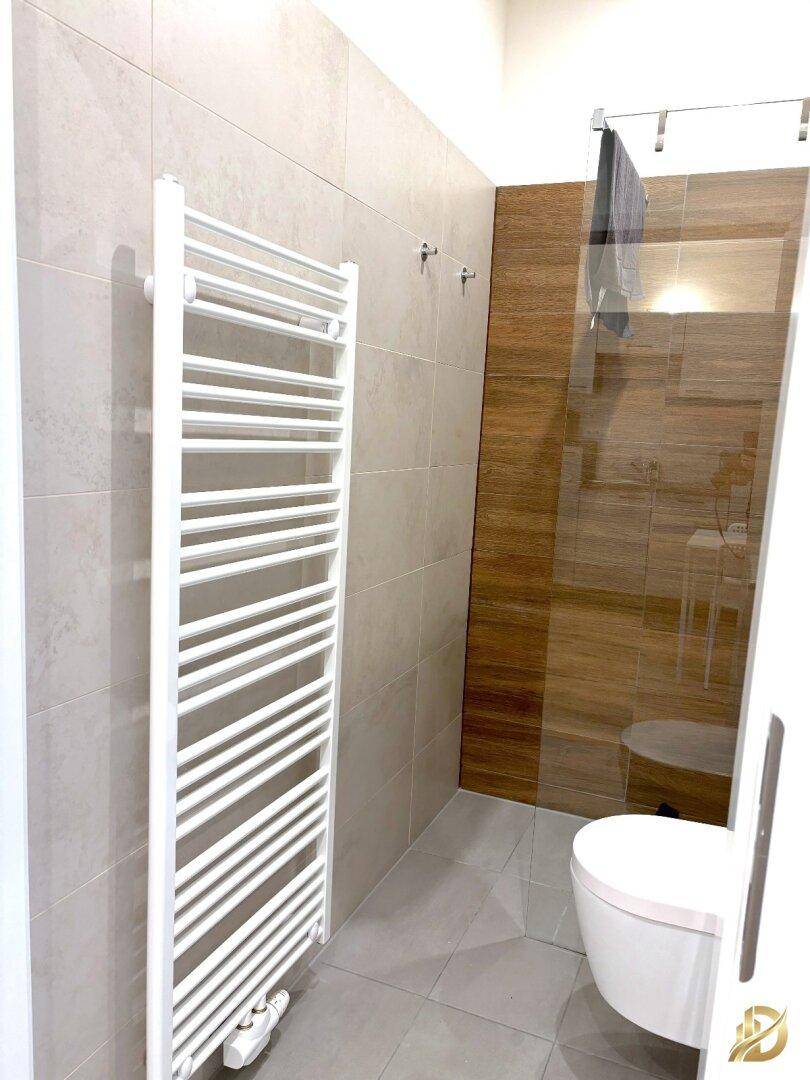 Helles Badezimmer mit Handtuchheizkörper, Dusche und modernen Fliesen.