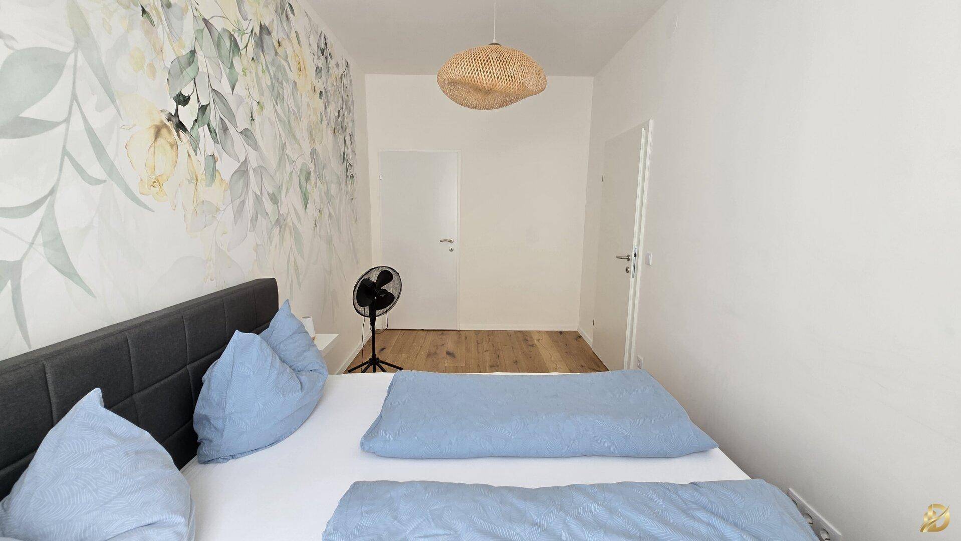 Modernes Schlafzimmer mit Doppelbett und floraler Wanddekoration, bietet eine ruhige und helle Atmosphäre.