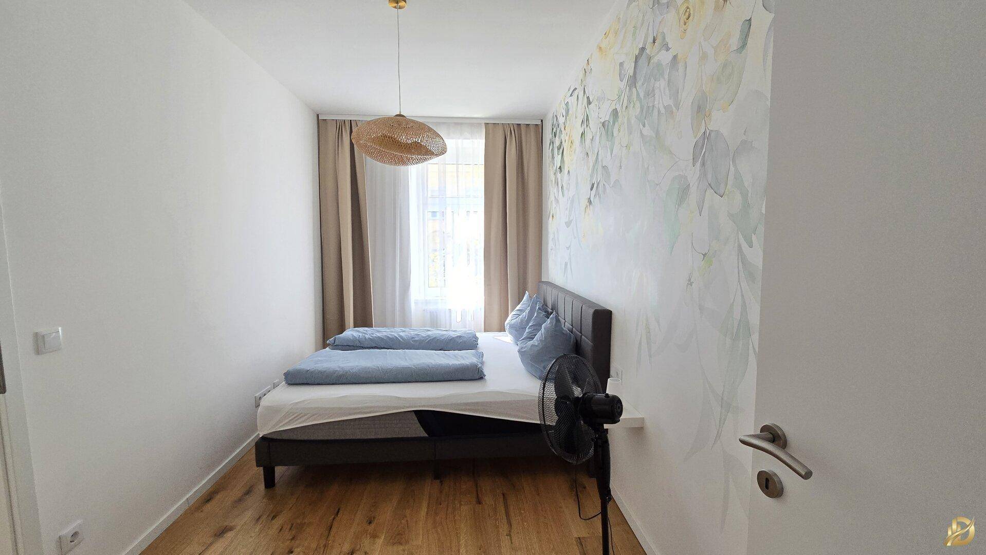 Helles Schlafzimmer mit Doppelbett, Holzboden und floraler Wanddekoration, modern und einladend.