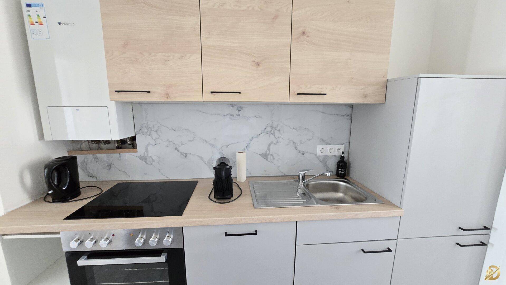 Moderne Küchenzeile mit hellen Holz- und Grautönen, Induktionskochfeld und Spüle, effizient gestaltet.