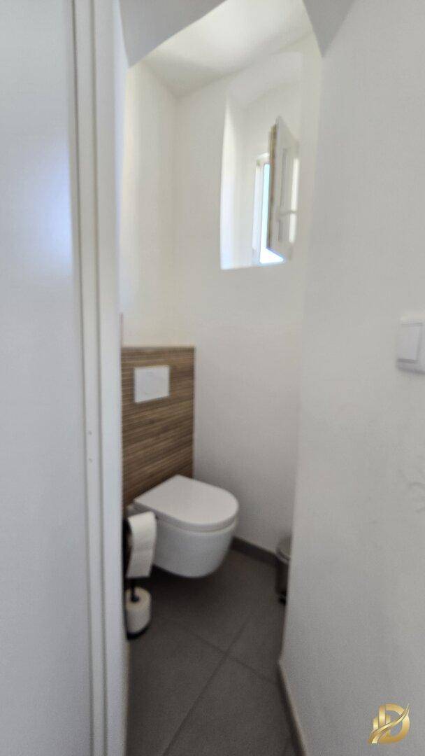 Kleines Gäste-WC mit wandhängender Toilette und Fenster, in schlichtem Design gehalten.