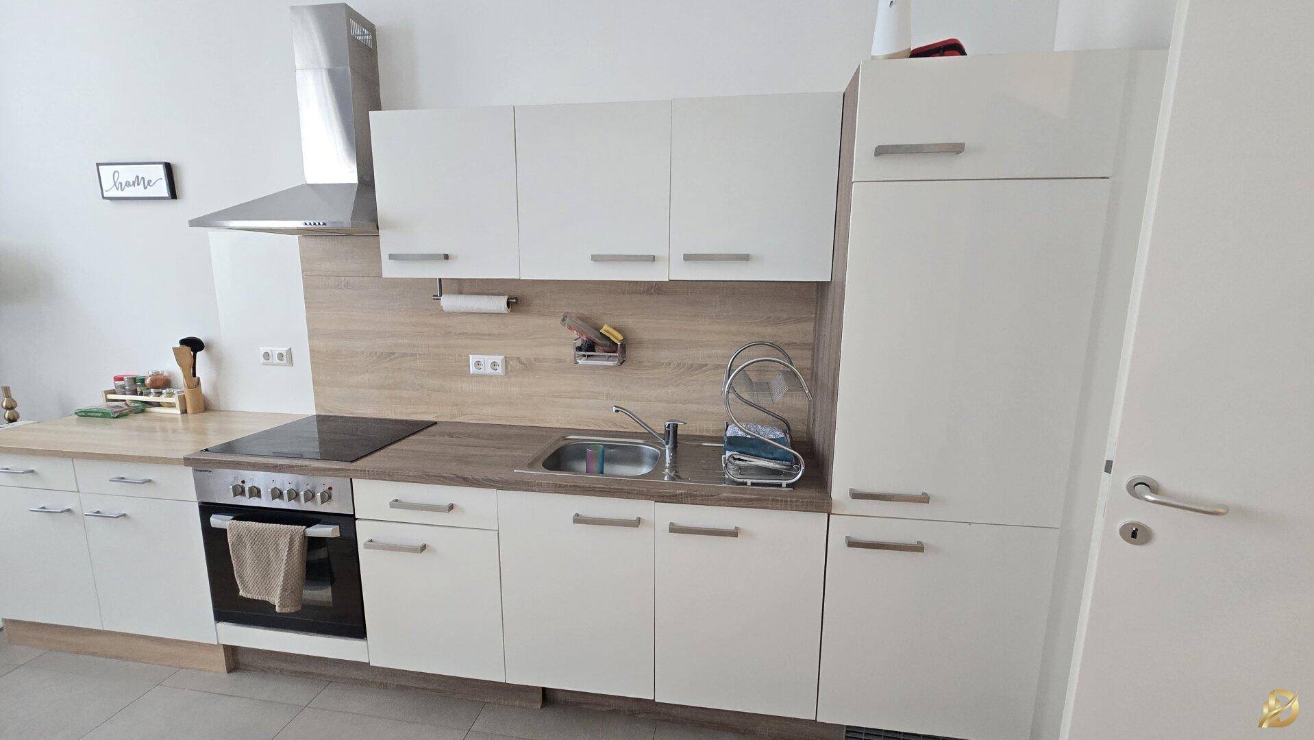 Funktionale Einbauküche mit weißen Schränken, Holzoptik-Arbeitsplatte und integriertem Kochfeld.