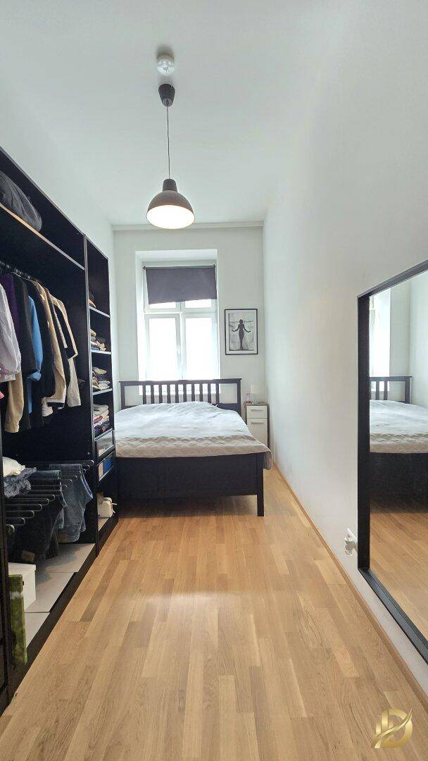 Helles Schlafzimmer mit Holzbett, offenem Kleiderschrank und großem Spiegel, mit Parkettboden.