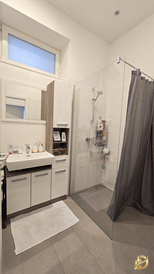 Modernes Badezimmer mit Dusche, Waschbeckenunterschrank und Fenster für Tageslicht.
