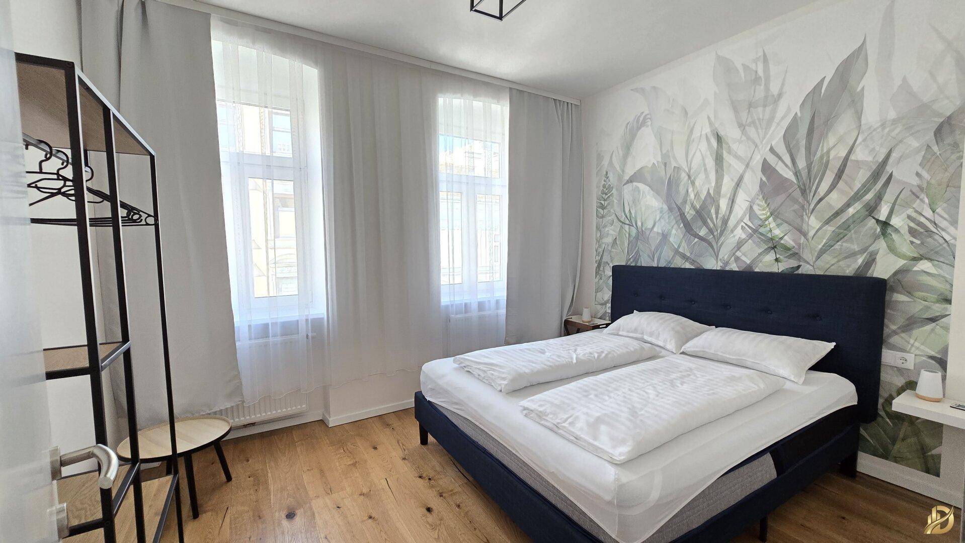 Helles Schlafzimmer mit Doppelbett, Holzboden und dekorativer Wandtapete.