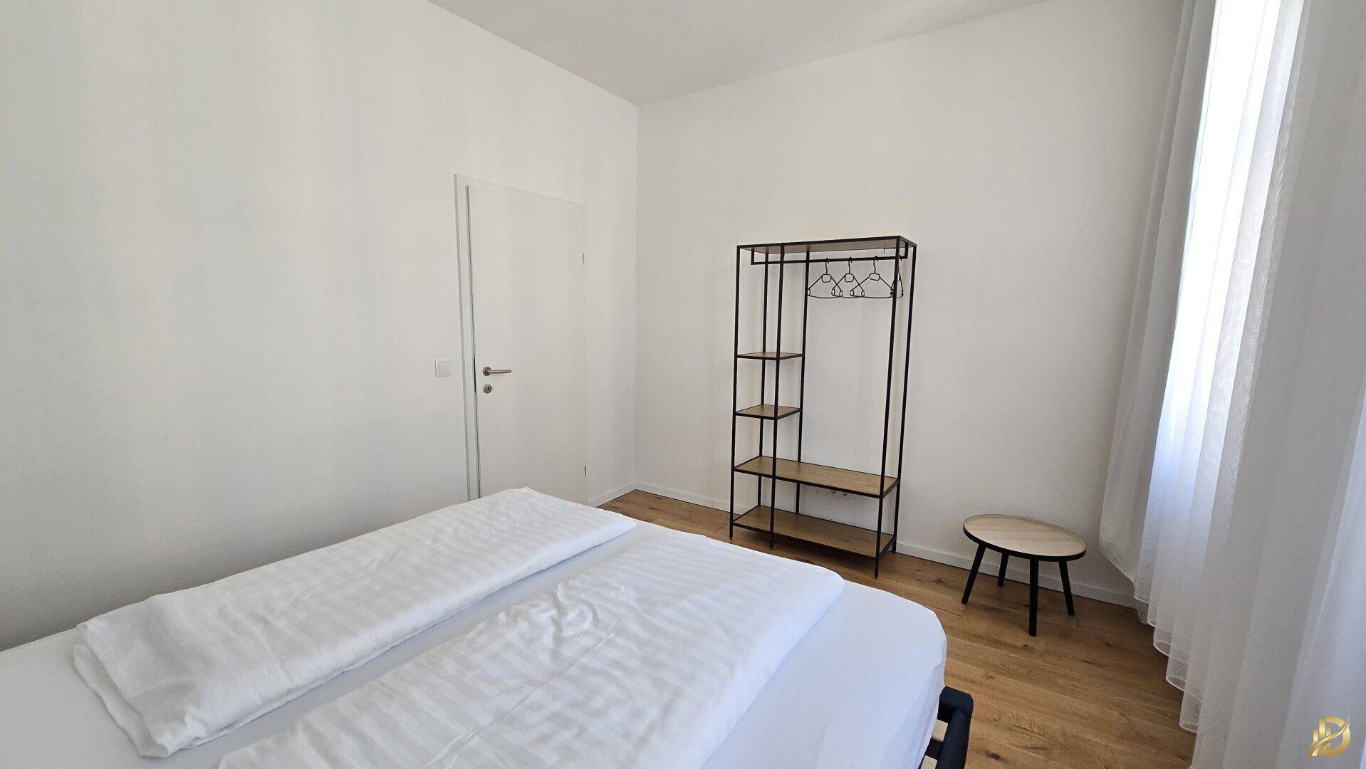 Schlafzimmer mit Holzboden, weiß gestrichenen Wänden und offenem Kleiderständer.