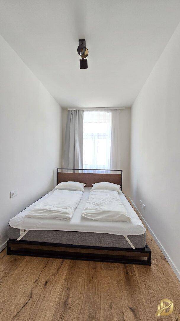 Schmaler Schlafbereich mit Doppelbett, Holzboden und Fenster.