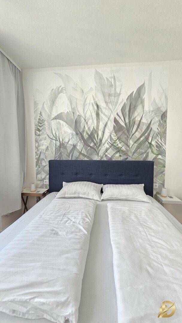Schlafzimmer mit Doppelbett und dekorativer Wandtapete hinter dem Bett.