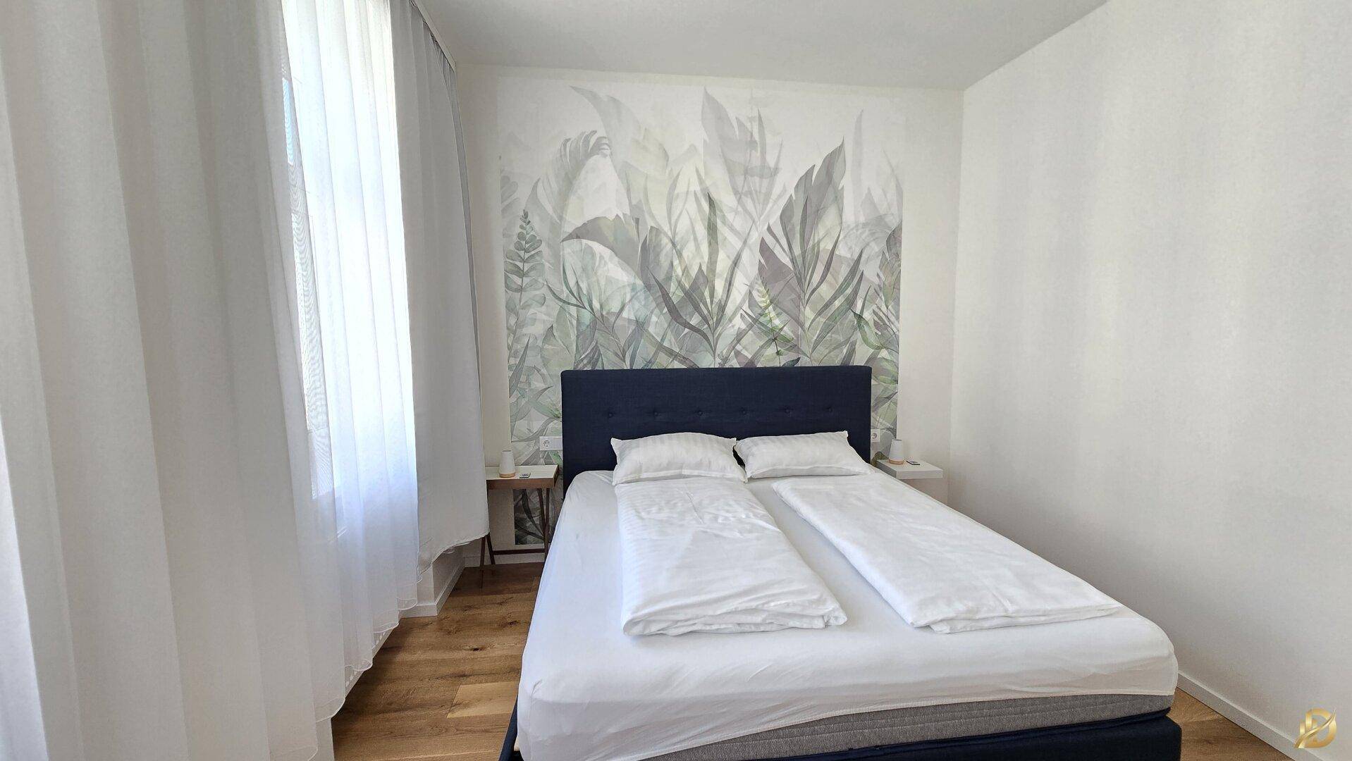 Helles Schlafzimmer mit Doppelbett, Holzboden und großen Fenstern.