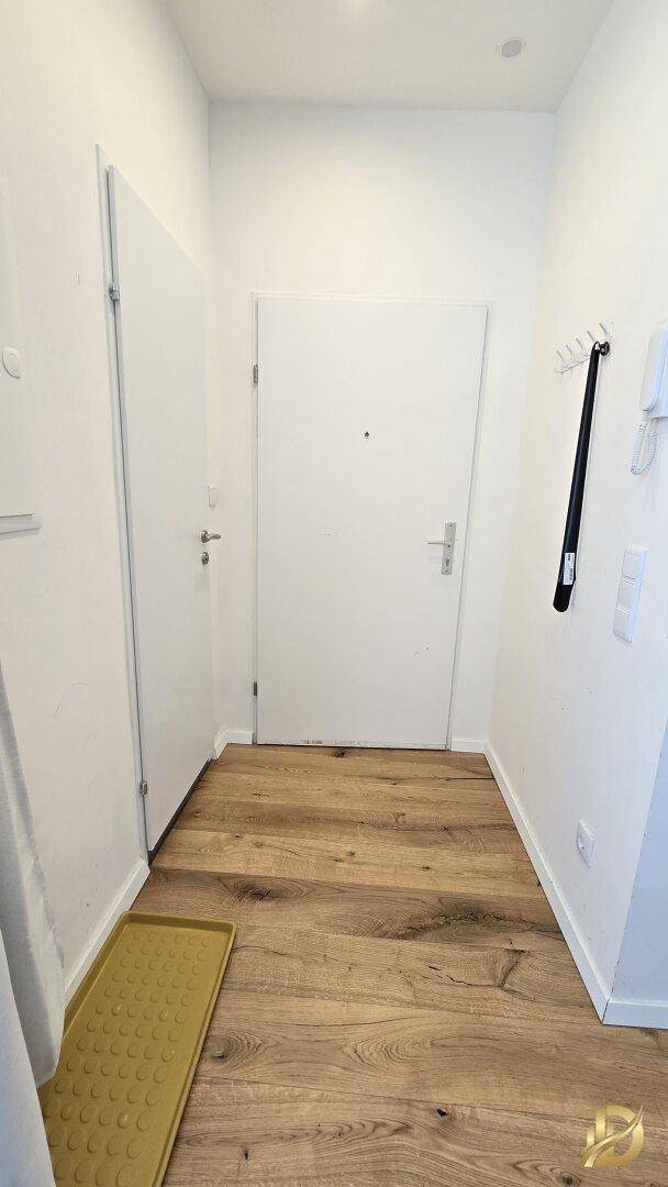 Heller Flur mit Holzboden und weißer Eingangstür.