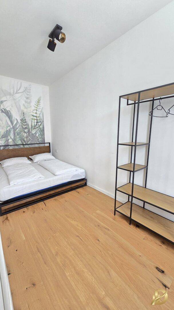 Schlafzimmer mit Holzboden, offenem Kleiderständer und dekorativer Wandtapete.