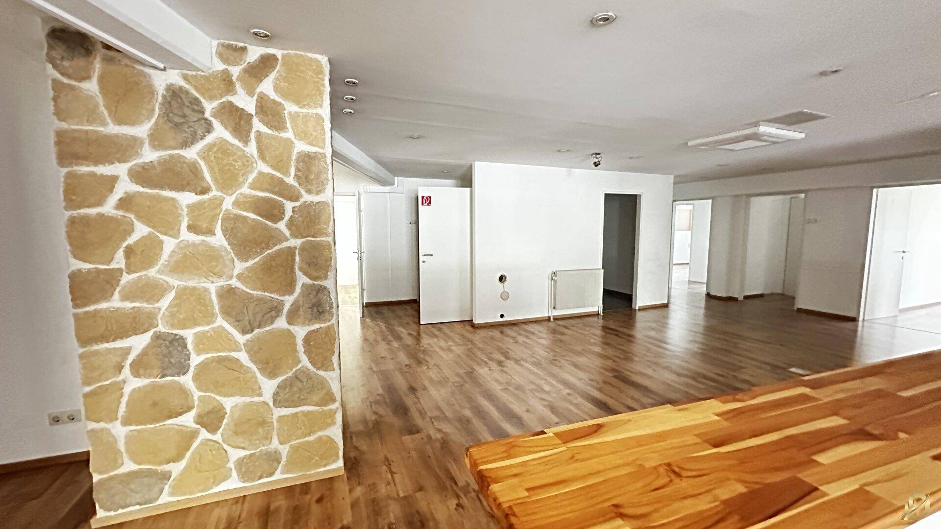 Geräumiger Gewerberaum mit Laminatboden und einer markanten Steinwand als gestalterisches Element.