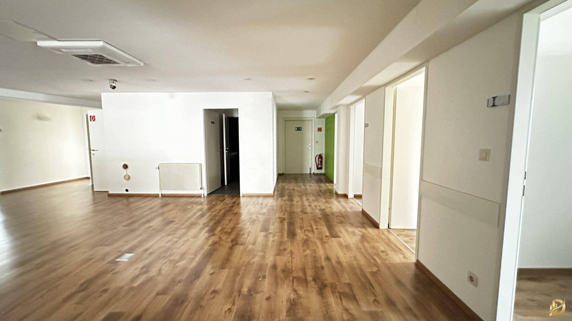 Offener Gewerberaum mit Laminatboden und Zugang zu mehreren Büros, ideal für flexible Nutzung.