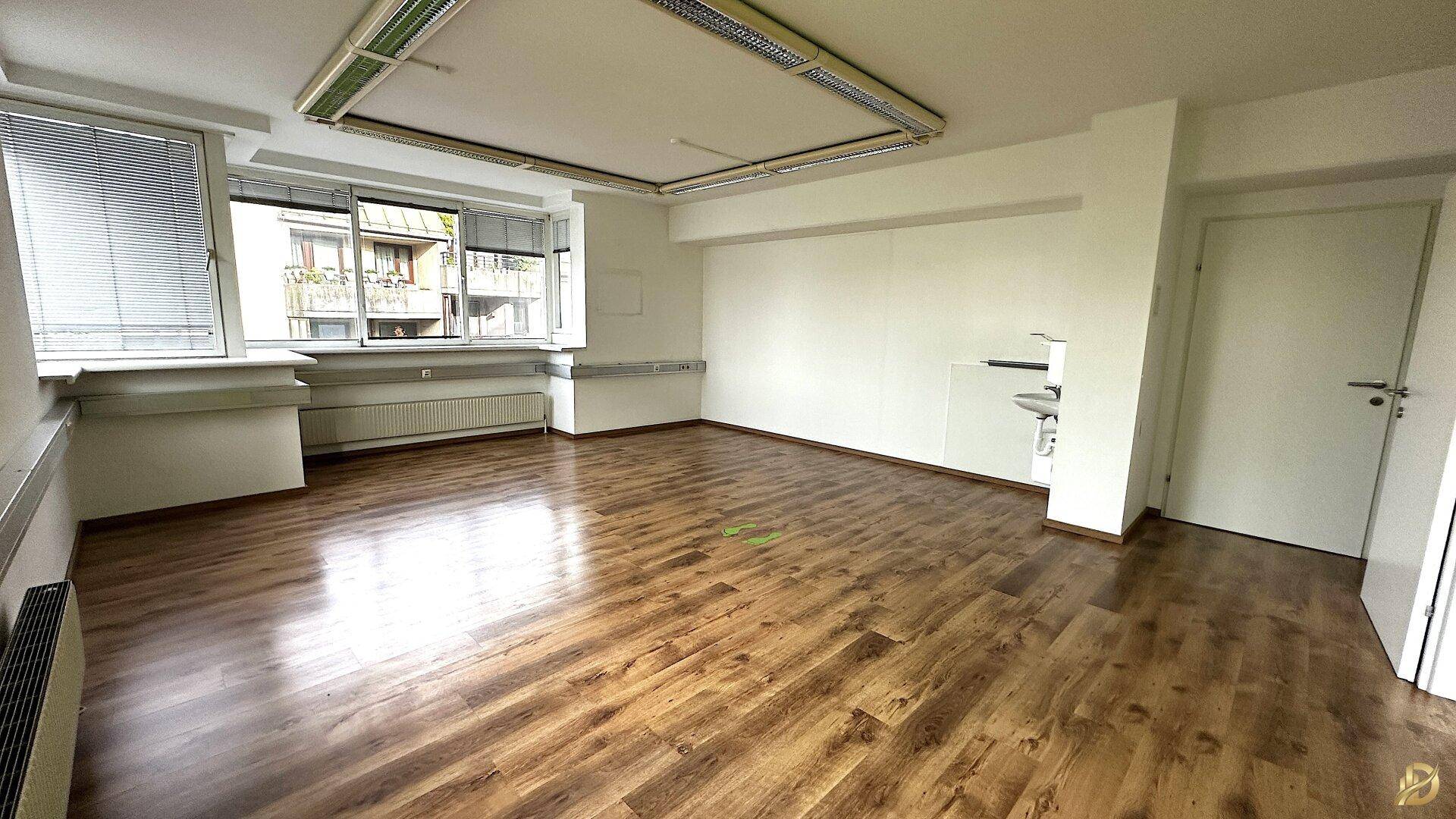 Büro mit Laminatboden, Fensterfront und einem Waschbecken, ideal für verschiedene Geschäftszwecke.