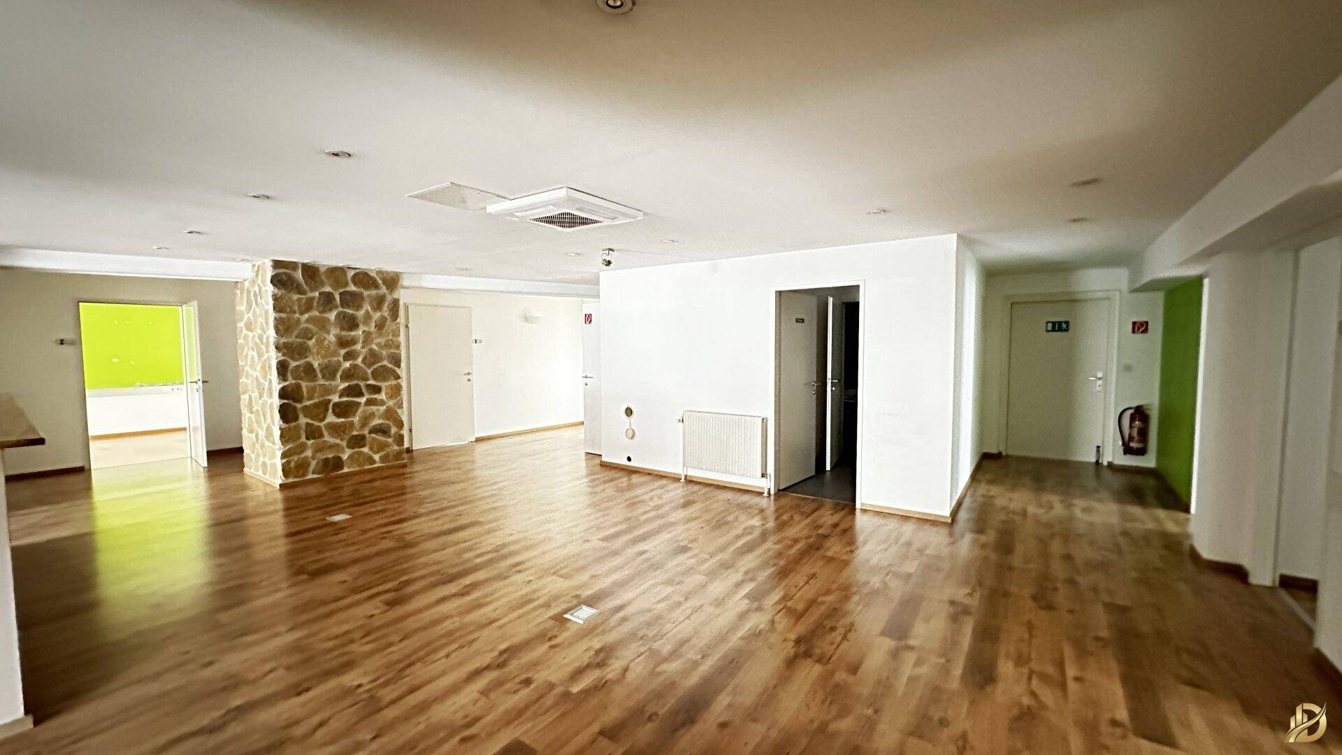 Heller Gewerberaum mit Laminatboden, Steinwand und Zugang zu weiteren Räumen.