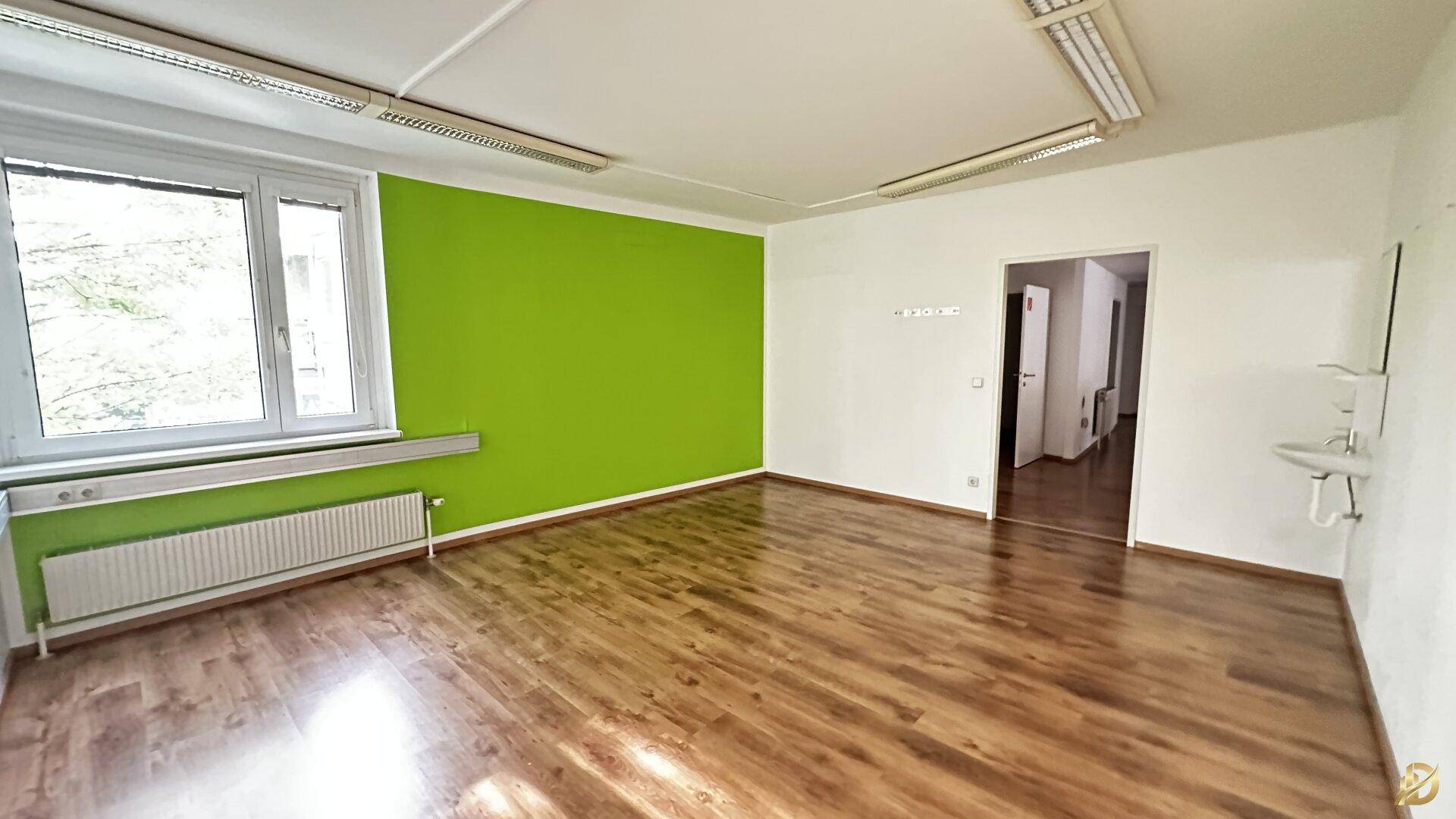 Büro mit Laminatboden, grüner Akzentwand, Fenster und einem Waschbecken, ideal für verschiedene Nutzungen.
