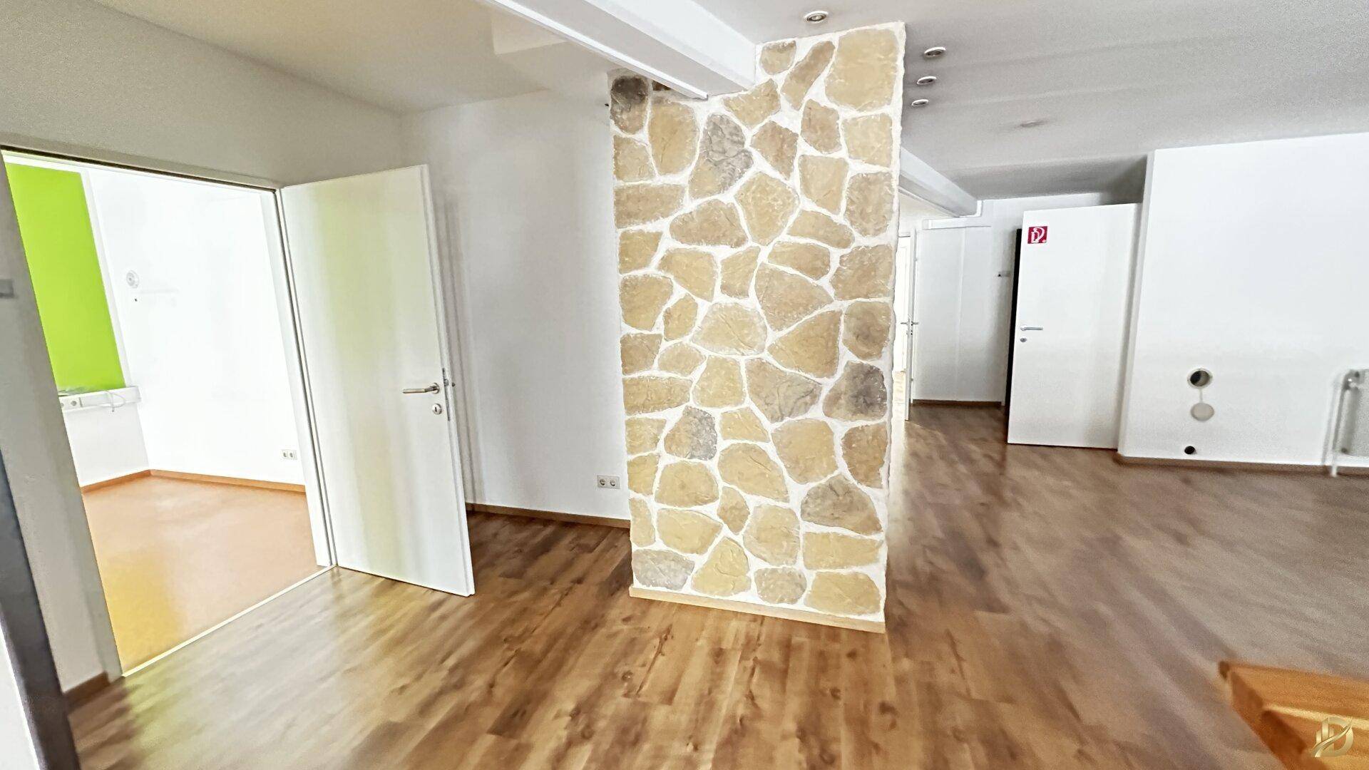Offener Gewerberaum mit Laminatboden und einer dekorativen Steinwand, die einen modernen Akzent setzt.