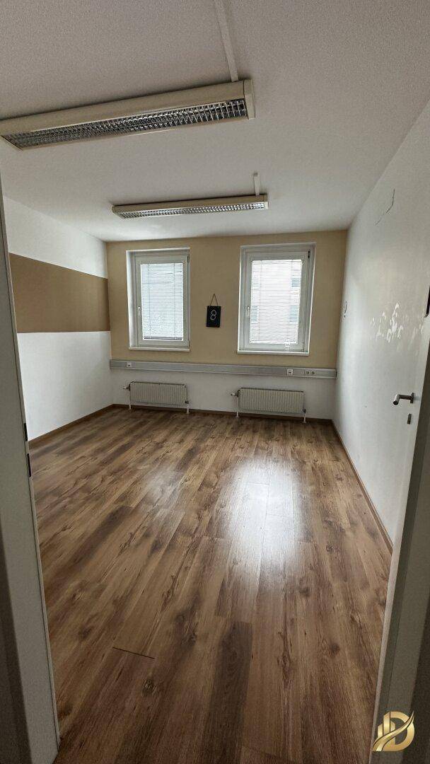 Büro mit Laminatboden, beiger Akzentwand und zwei Fenstern, die den Raum hell und freundlich machen.