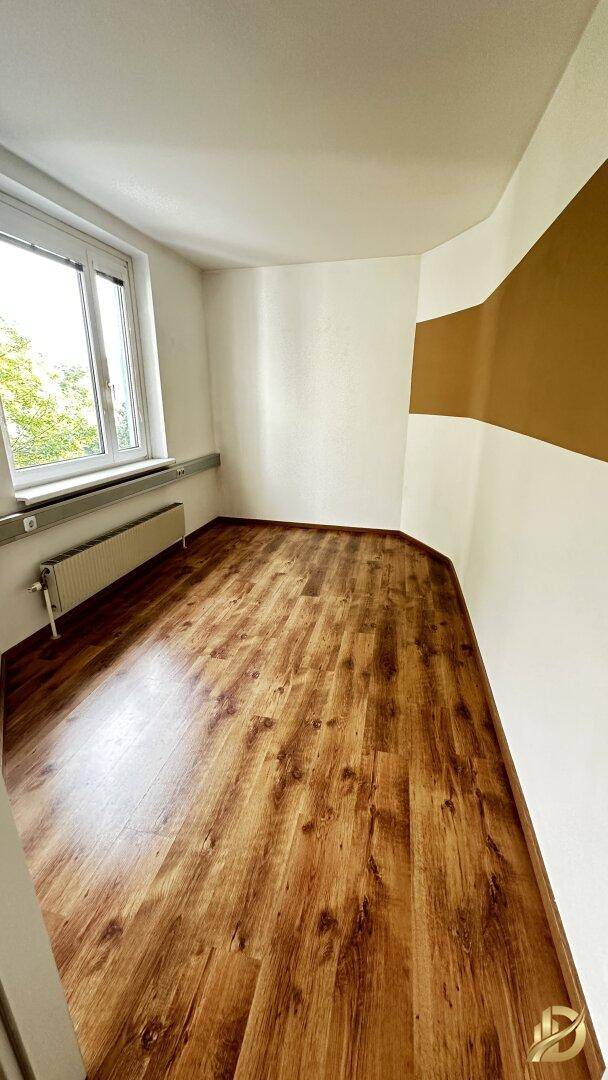 Büro mit Laminatboden, einer braunen Akzentwand und einem Fenster, das den Raum erhellt.