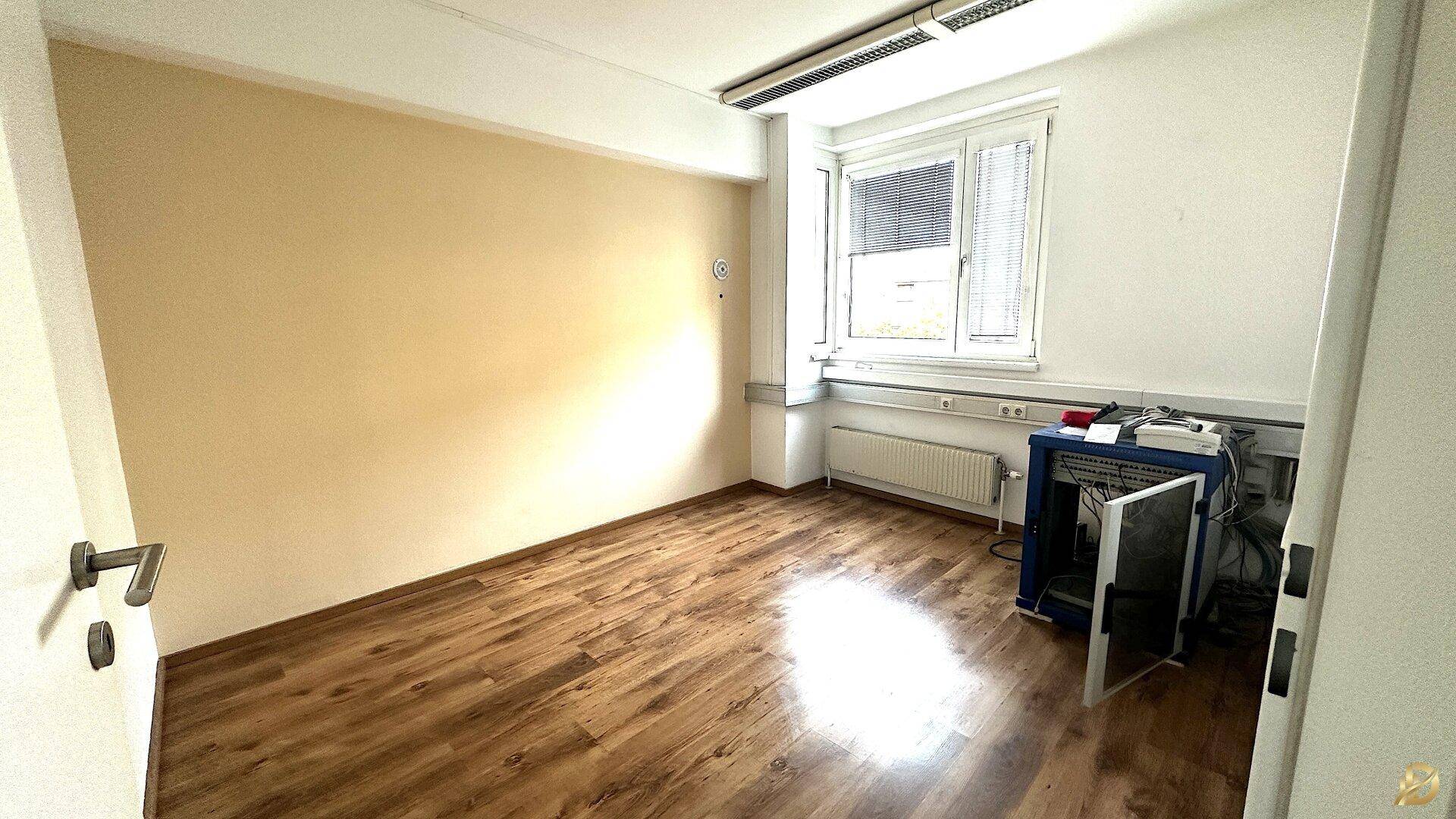 Einzelbüro mit Laminatboden, einer beigen Wand und einem Fenster, das ausreichend Tageslicht bietet.
