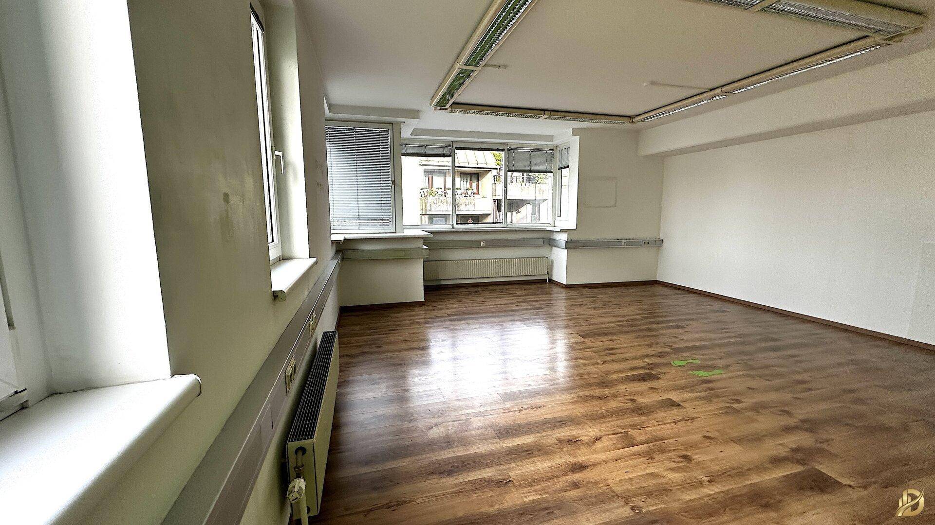 Büro mit Laminatboden und breiter Fensterfront, die viel Tageslicht hereinlässt und einen Ausblick bietet.