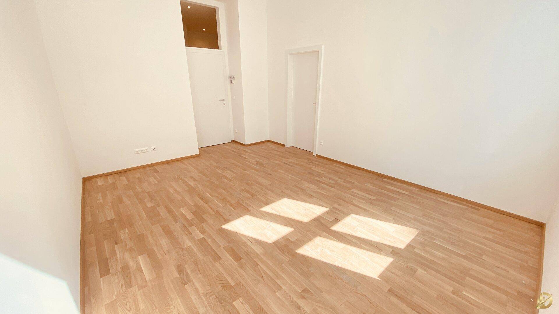Leeres Zimmer mit Holzboden und einer Tür, die zu einem weiteren Raum führt.