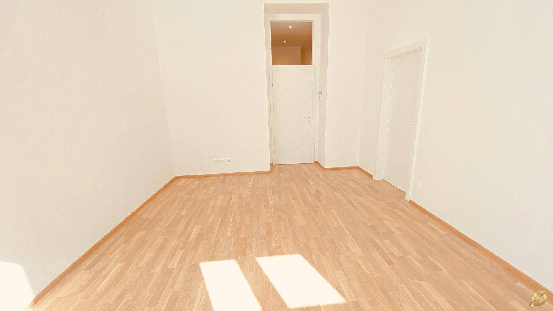 Leeres Zimmer mit Holzboden und einer Tür, die zu einem weiteren Raum führt.