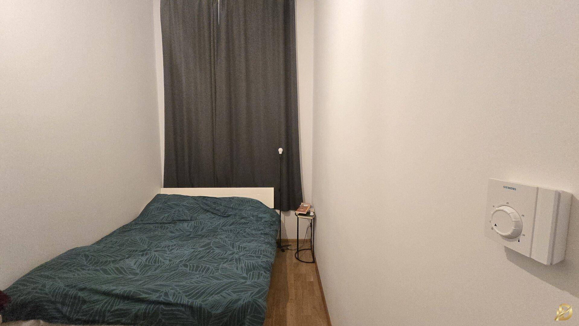 Schlafzimmer mit Einzelbett, dunklen Vorhängen und einem Heizungsthermostat an der Wand.