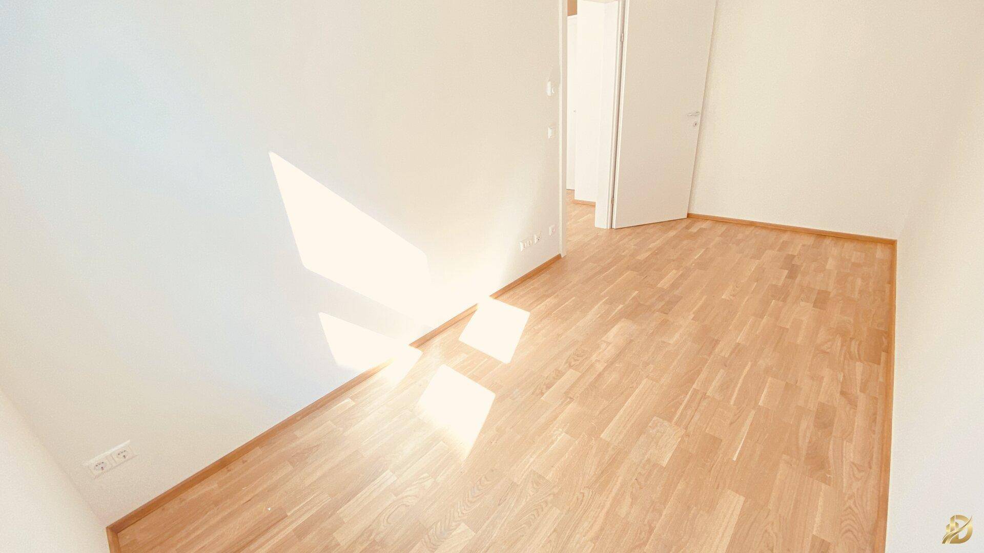 Leeres Zimmer mit Holzboden und viel Sonnenlicht, das durch die Tür fällt.