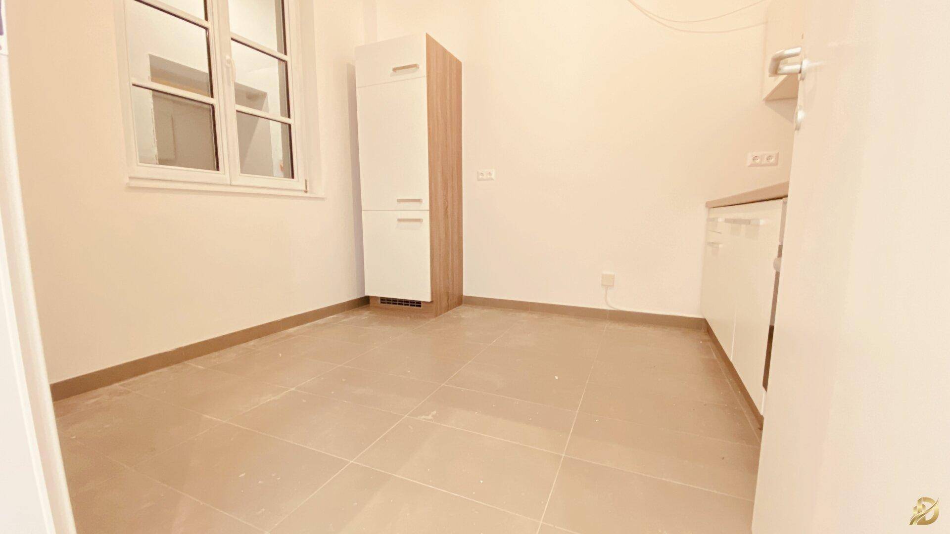 Kleine Küchenzeile mit Fenster, weißen Schränken und Fliesenboden.