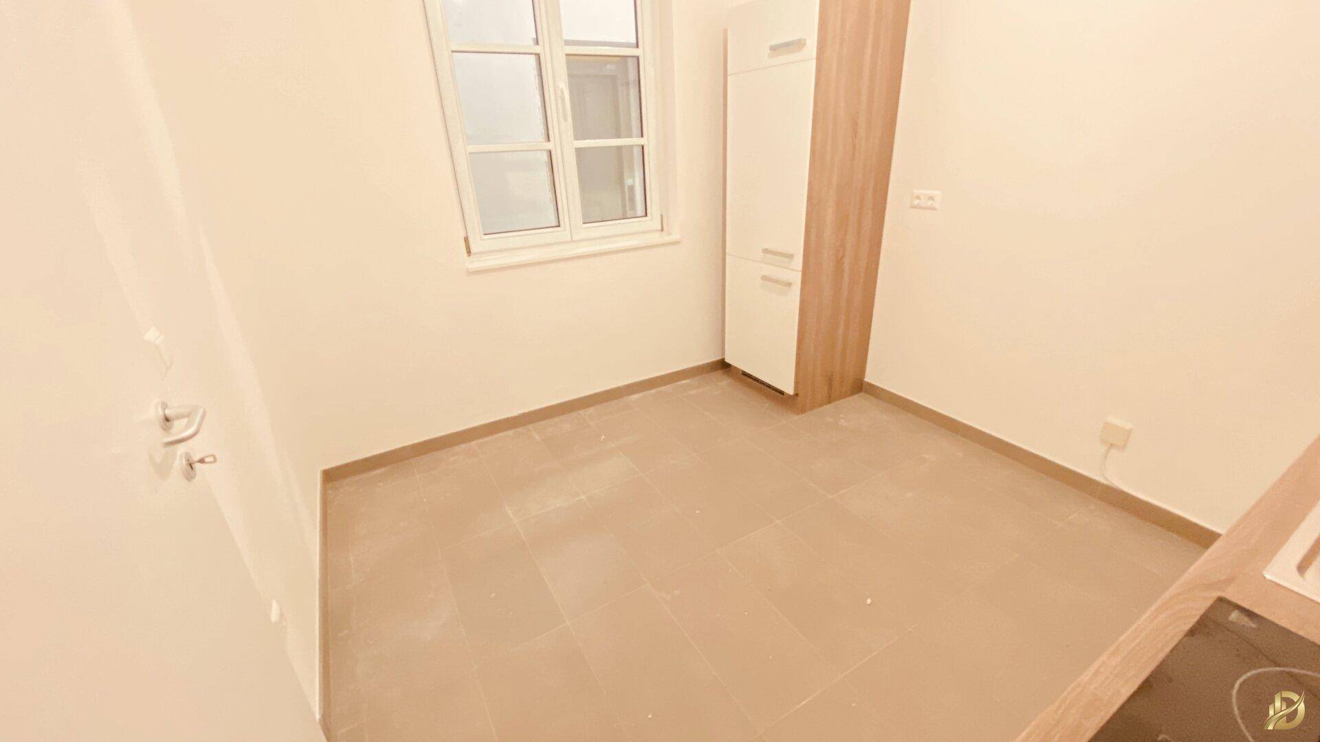 Kleine Küchenzeile mit Fenster, weißen Schränken und Fliesenboden.