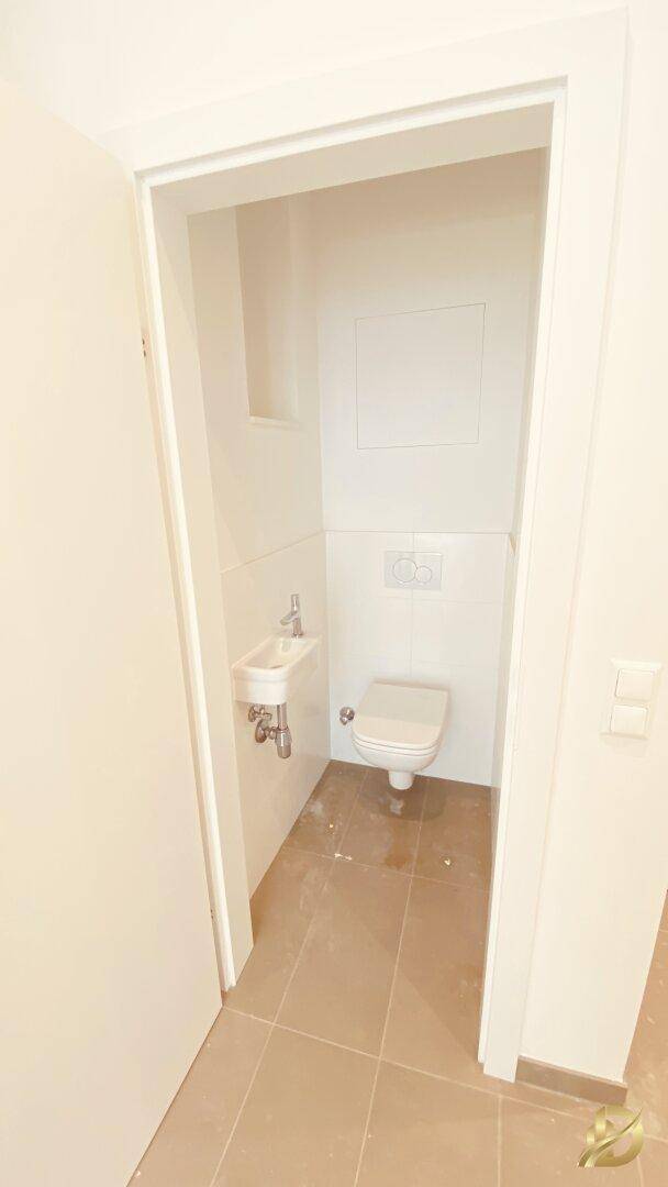 Separate Gästetoilette mit wandhängendem WC und kleinem Handwaschbecken.