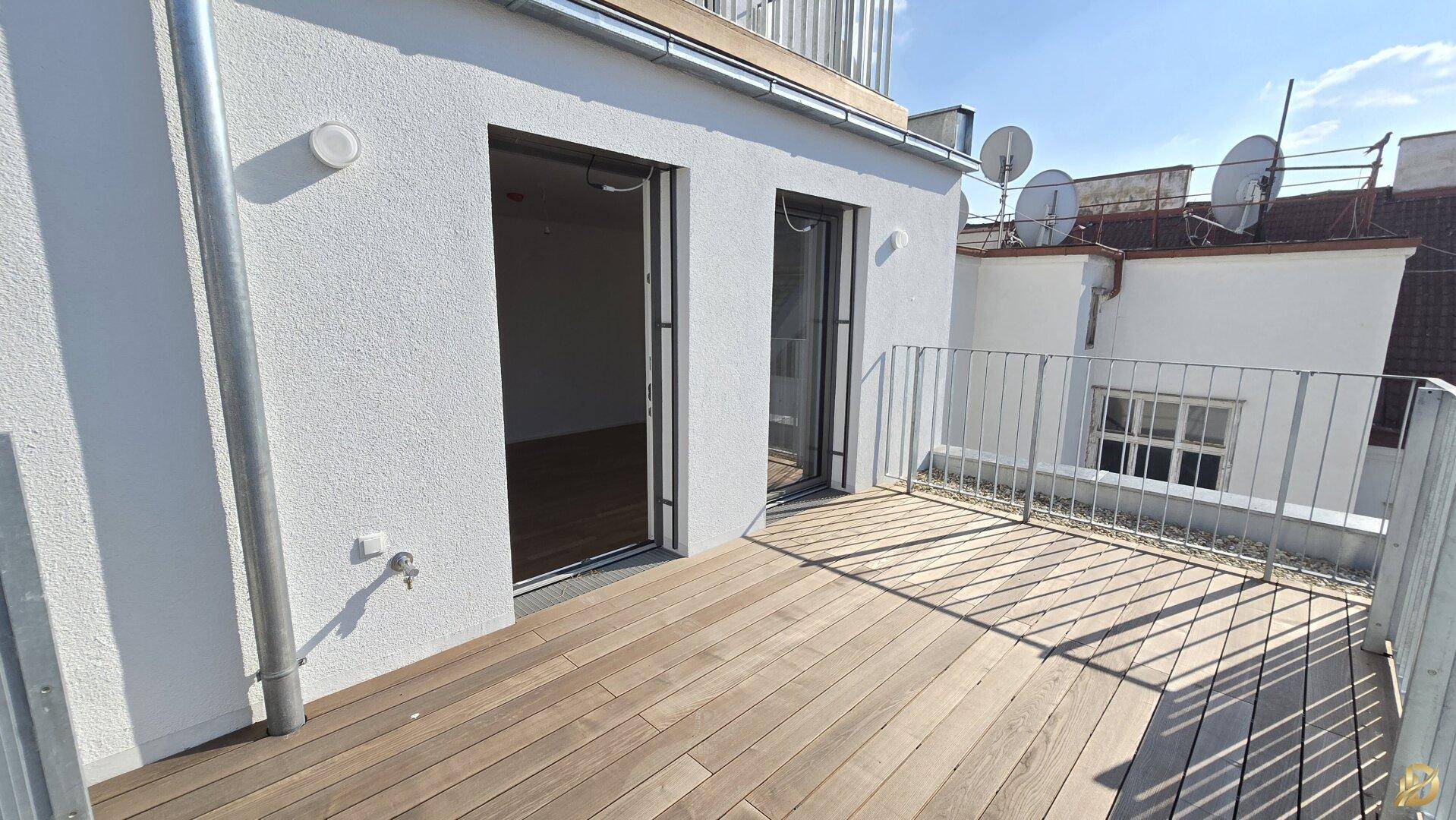 Sonniger Balkon mit Holzbelag und modernem Geländer, bietet einen Blick auf die Dächer der Stadt.