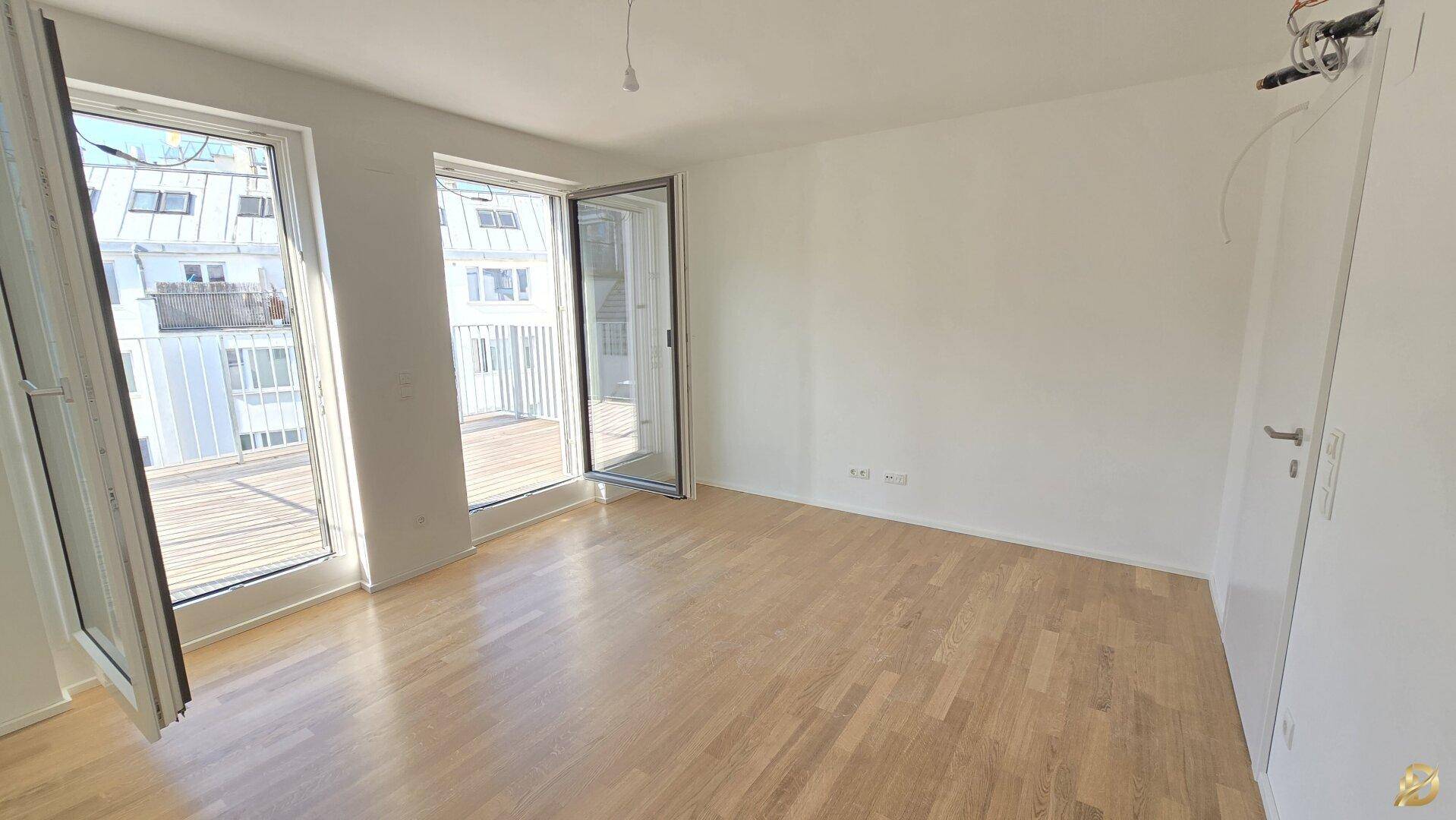 Lichtdurchfluteter Raum mit hellem Parkettboden und offenem Zugang zu einem sonnigen Balkon.