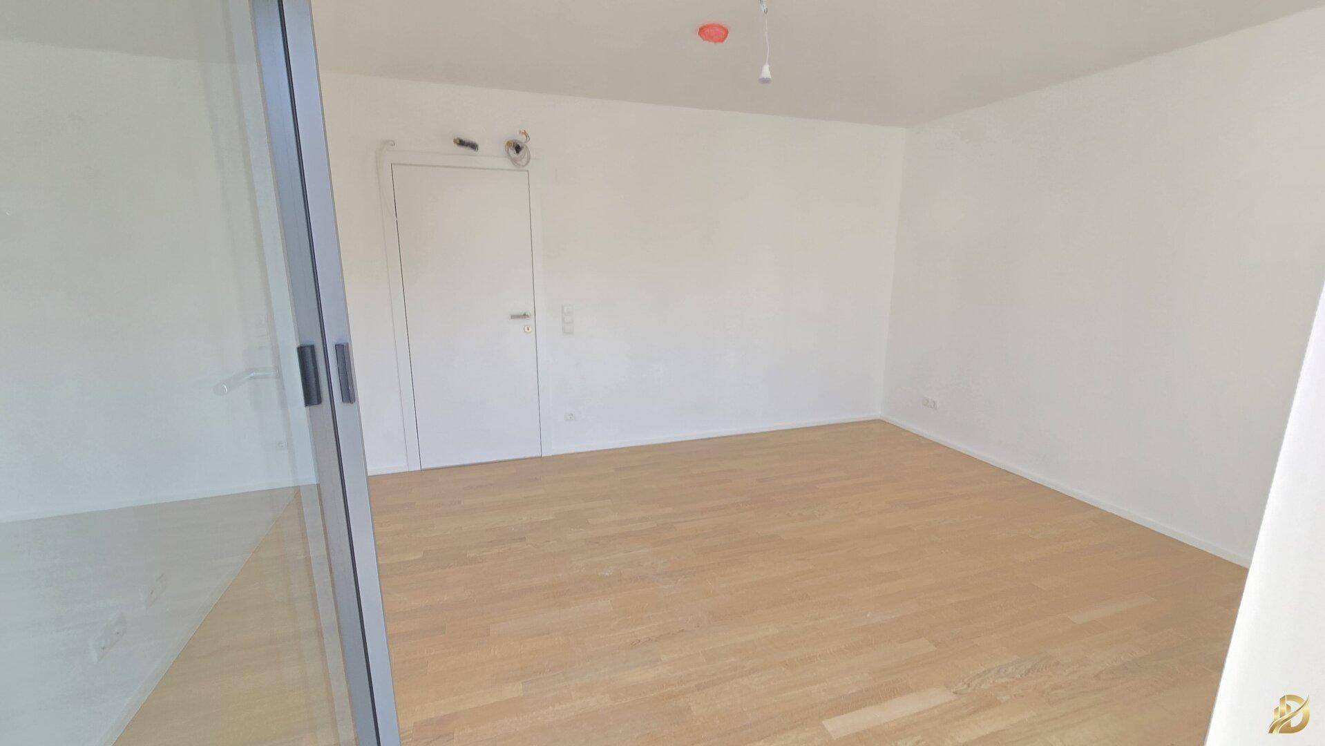 Leeres Zimmer mit hellem Parkettboden und weißer Tür, bereit für individuelle Gestaltung.