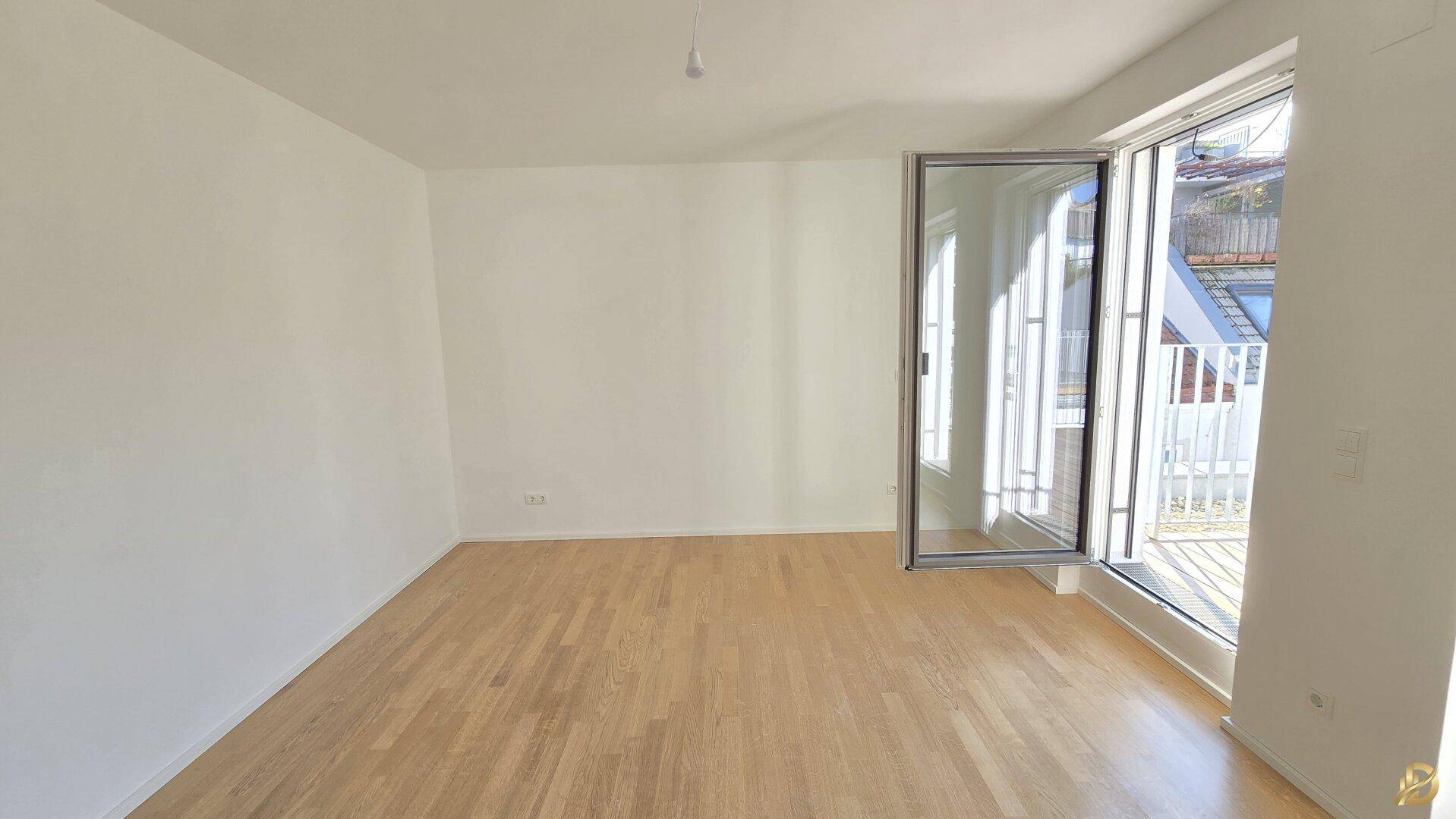 Heller Raum mit Parkettboden und offenem Fenster, das Zugang zu einem Außenbereich bietet.